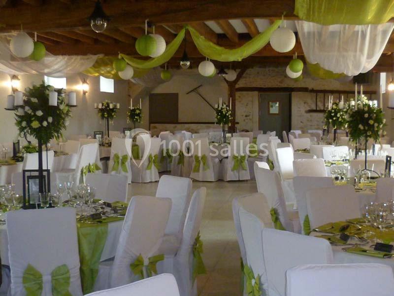 Salle de réception décorée avec des chaises blanches ornées de nœuds verts, tables dressées et guirlandes suspendues.