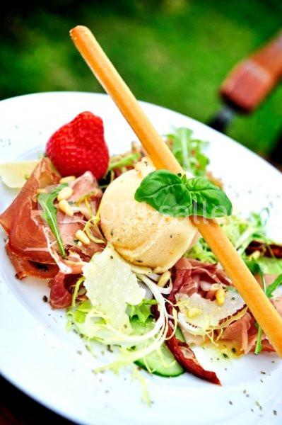 Assiette de salade composée avec jambon cru, fromage, fraise, grissini et feuilles de basilic, servie en extérieur.