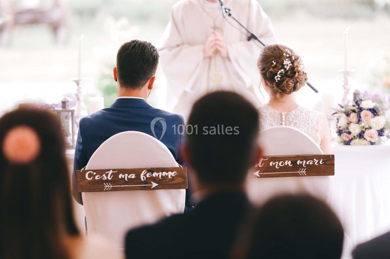 Un couple assis de dos lors d'une cérémonie de mariage, avec des panneaux indiquant ’C'est ma femme’ et ’C'est mon mari’.