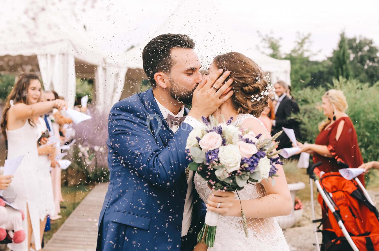 Un couple de mariés s'embrasse sous une pluie de confettis, entouré d'invités lors d'une cérémonie en plein air.