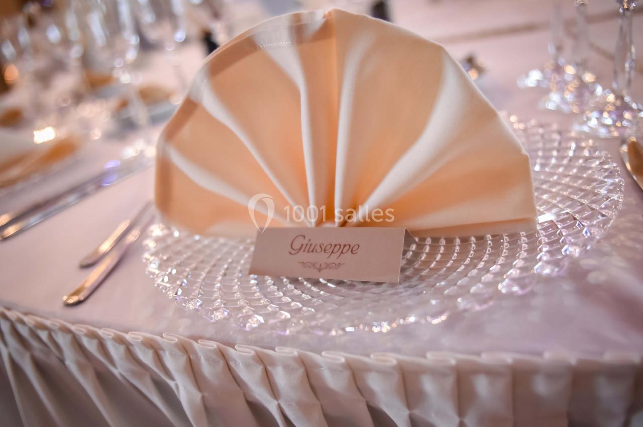 Serviette pliée en éventail sur une assiette en verre, avec un marque-place portant le prénom ’Giuseppe’.