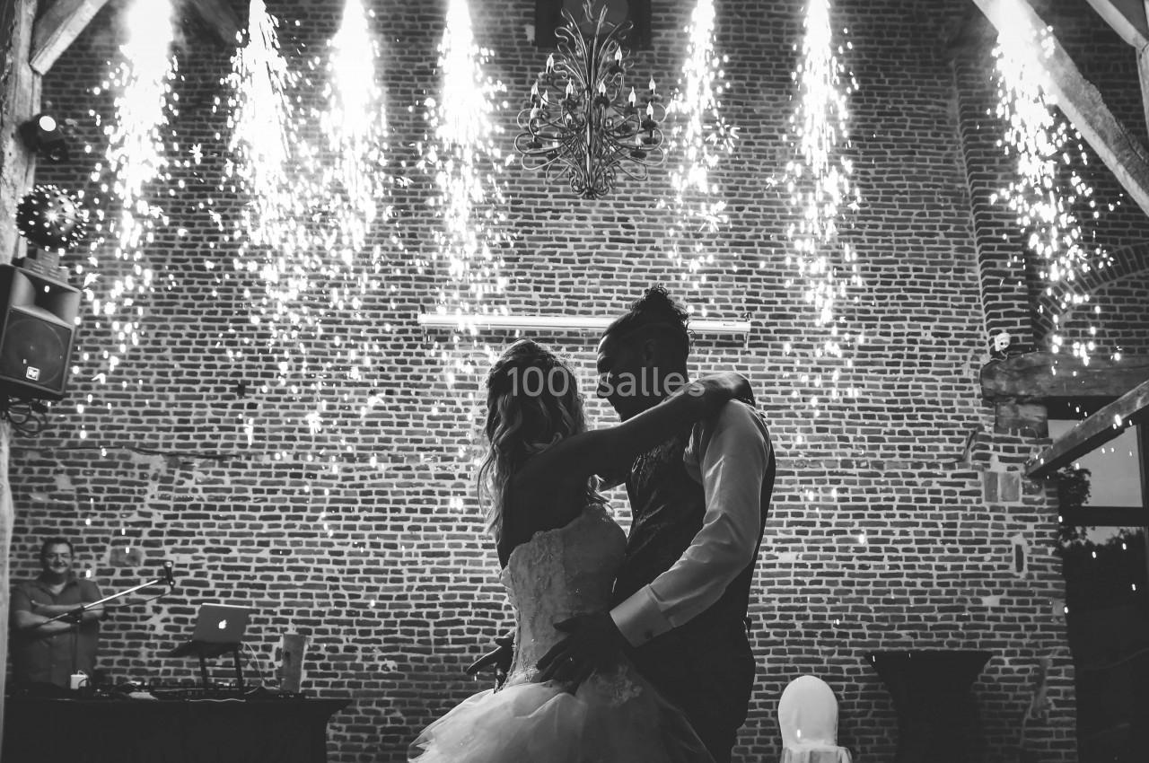 Un couple danse sous des étincelles dans une salle en briques, éclairée par une lumière tamisée.