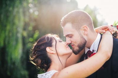 Un couple en tenue de mariage se tient la main dans un jardin baigné par une lumière douce au coucher du soleil.