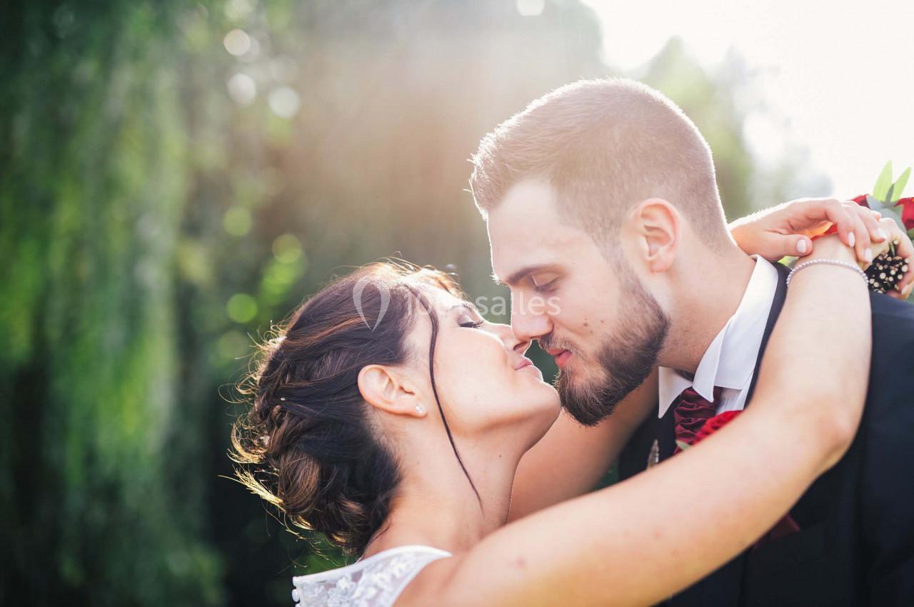 Un couple habillé élégamment s'embrasse tendrement dans un jardin ensoleillé.