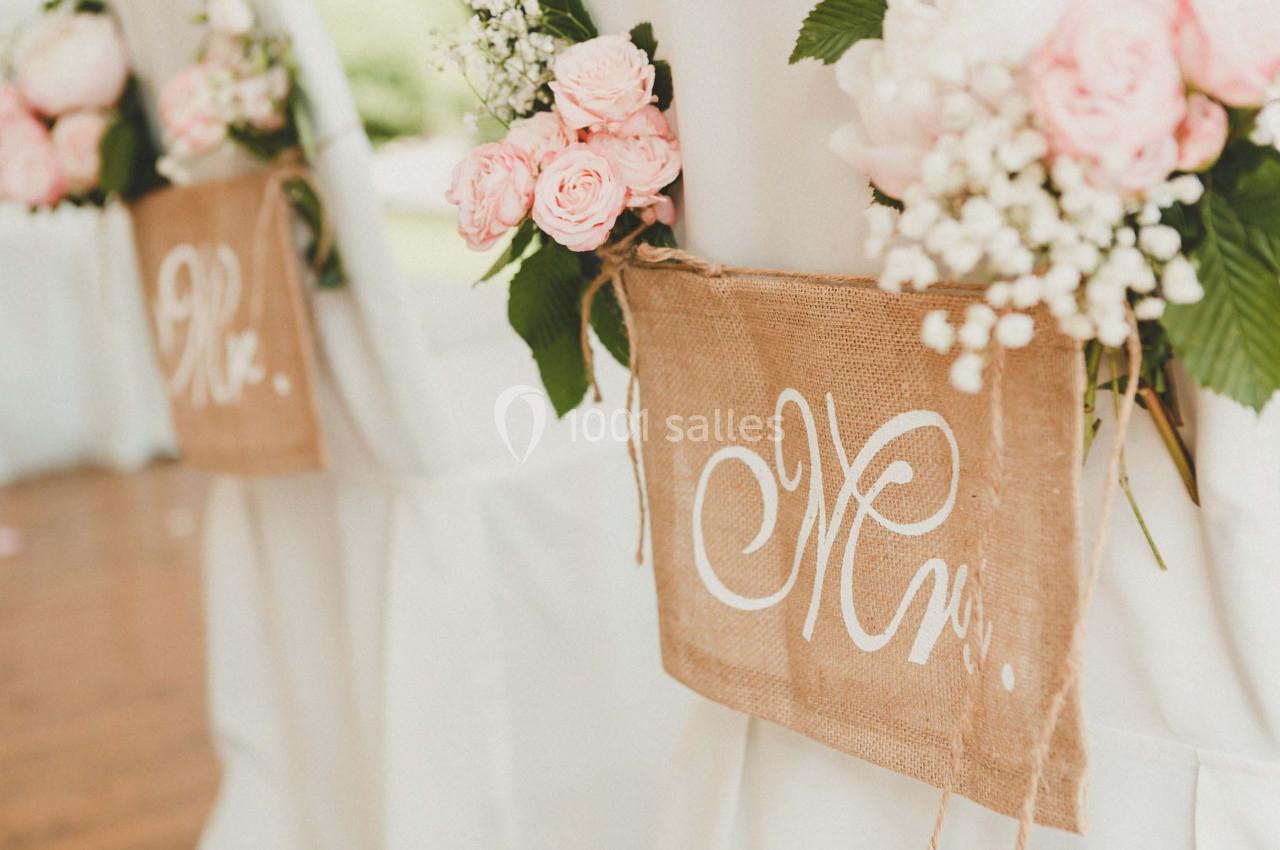 Chaises décorées de roses roses, gypsophiles et panneaux en toile de jute avec inscriptions manuscrites.