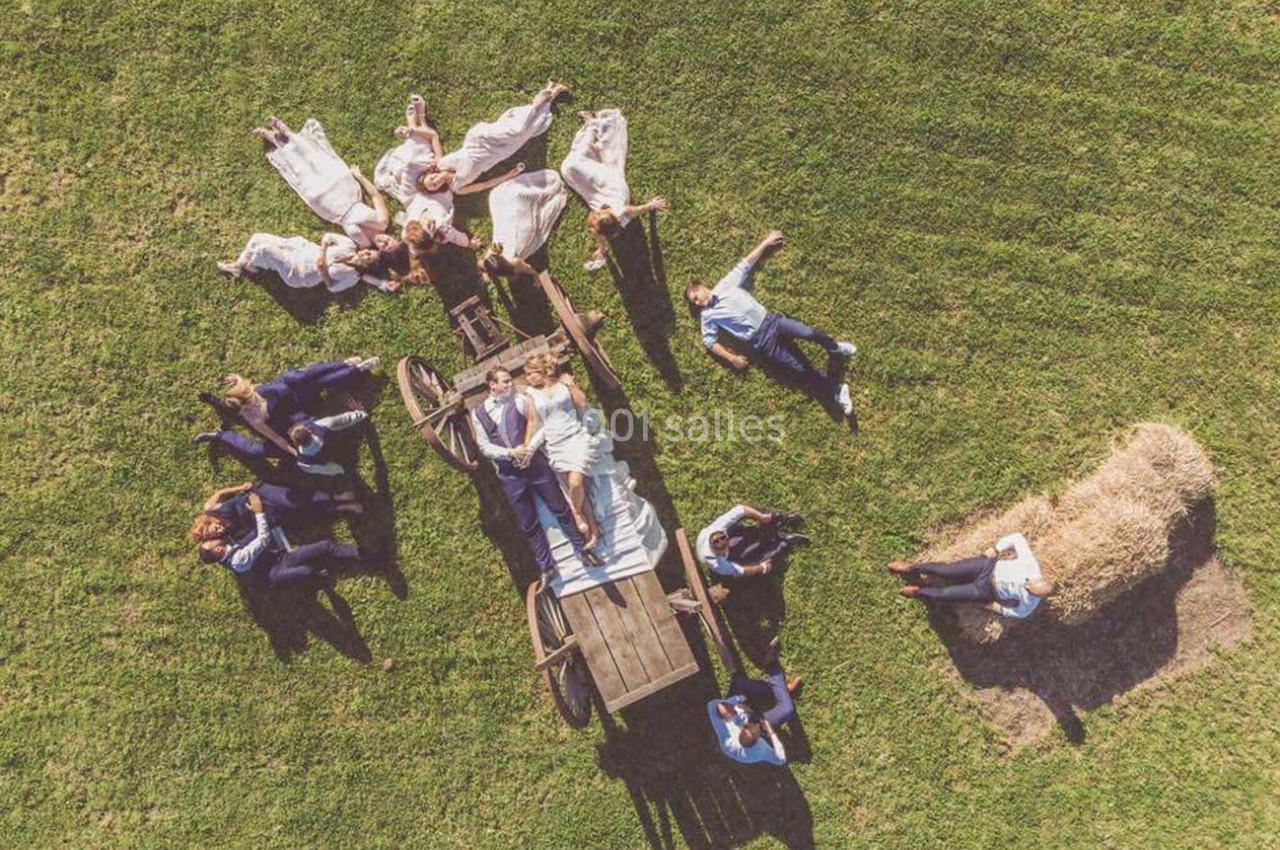 Vue aérienne d'un groupe de personnes allongées sur l'herbe autour d'une charrette en bois, près d'une botte de foin.