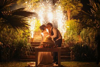 Un couple en tenue de mariage se tient la main dans un jardin baigné par une lumière douce au coucher du soleil.