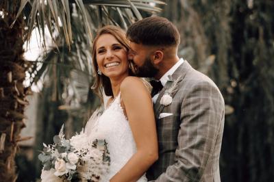 Un couple en tenue de mariage se tient la main dans un jardin baigné par une lumière douce au coucher du soleil.
