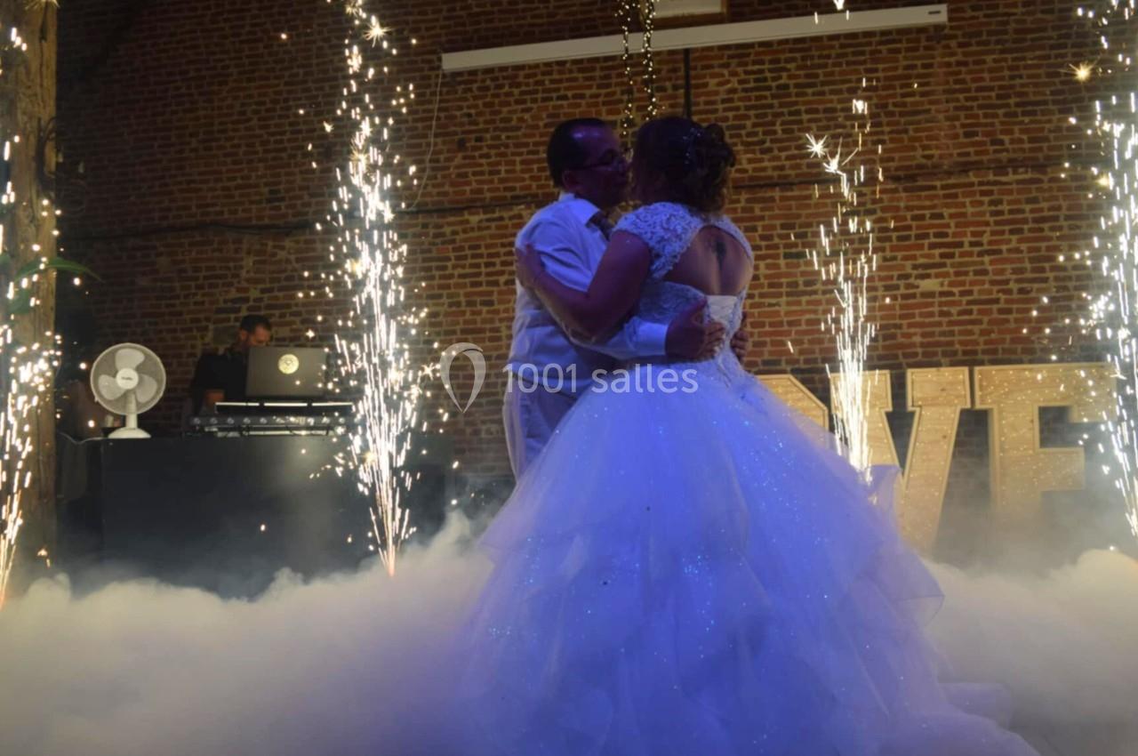 Un couple danse au milieu de fumée et de gerbes d'étincelles, dans une salle en briques avec un DJ en arrière-plan.
