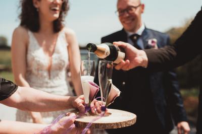 Un couple en tenue de mariage se tient la main dans un jardin baigné par une lumière douce au coucher du soleil.