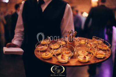 Plateau de bouchées apéritives variées présentées sur un napperon blanc, tenu par une personne en chemise blanche.