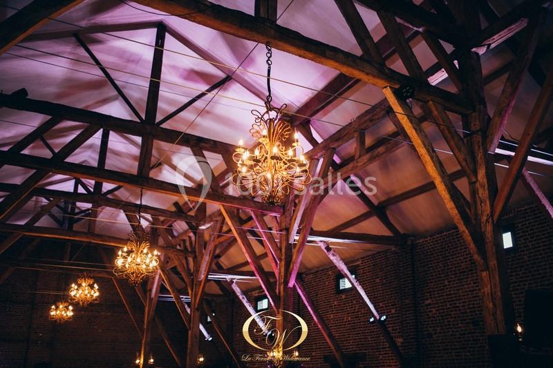 Plafond en poutres apparentes avec des lustres suspendus diffusant une lumière chaleureuse dans une grande salle.