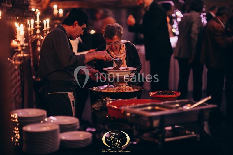 Un serveur sert un plat à une femme dans un buffet éclairé par des bougies, avec des convives en arrière-plan.