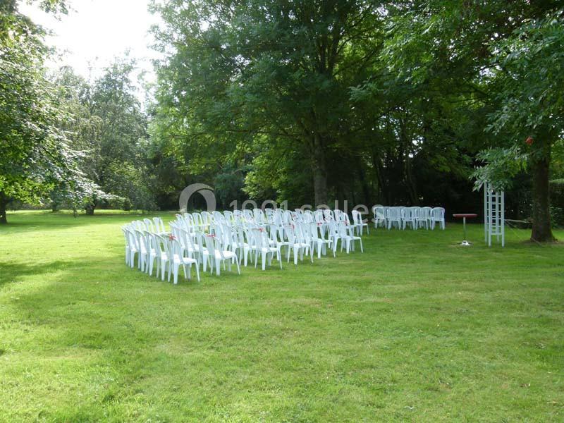 Chaises blanches disposées en rangées sur une pelouse verdoyante, entourées d'arbres dans un cadre extérieur paisible.