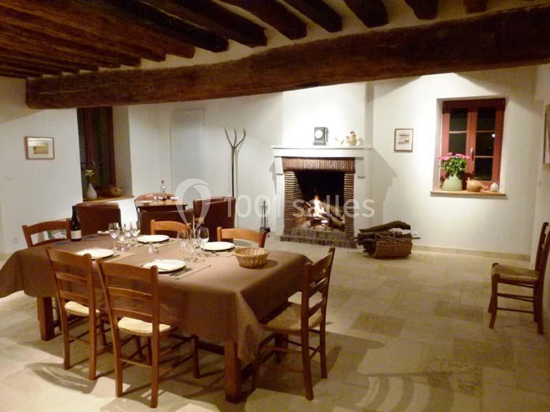 Salle à manger chaleureuse avec une cheminée allumée, des tables dressées et des poutres apparentes au plafond.
