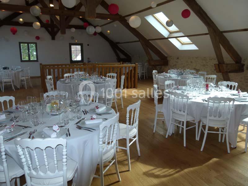 Salle de réception lumineuse avec tables rondes dressées, chaises blanches et décorations suspendues sous un plafond en…
