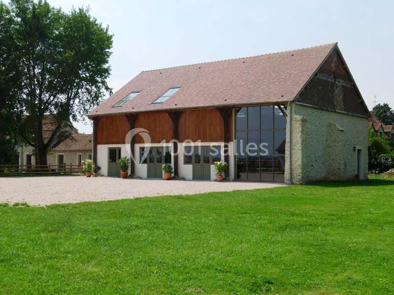 Bâtiment rénové avec façade en verre et bois, entouré de pelouse et d'arbres, par une journée ensoleillée.