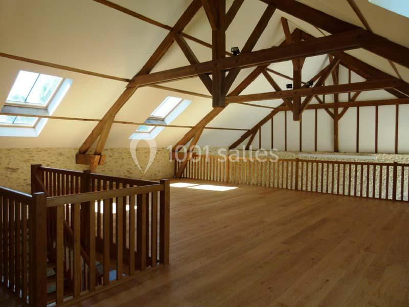 Vue d'un grenier aménagé avec poutres apparentes, parquet en bois clair et plusieurs fenêtres de toit.