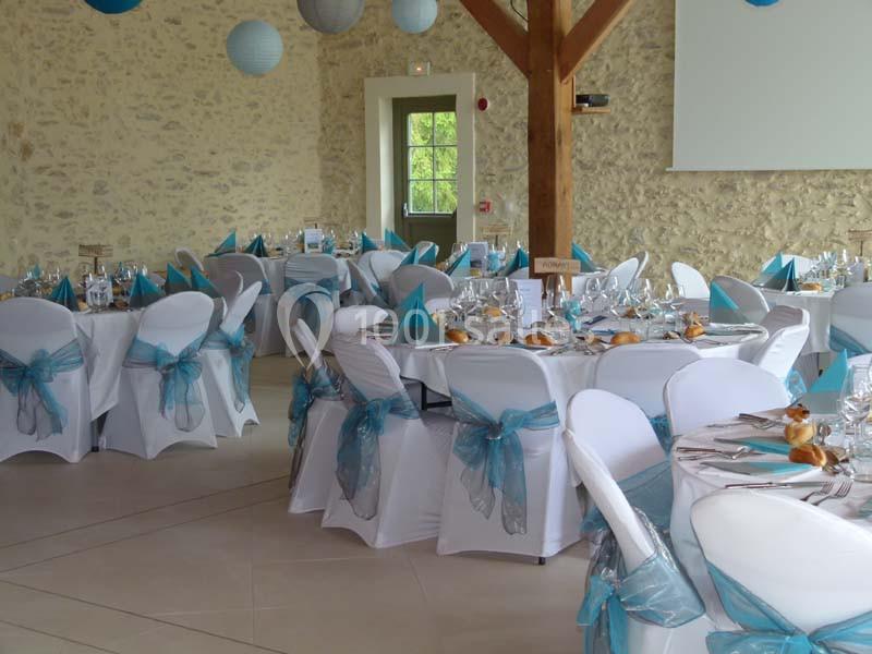 Salle de réception décorée avec des nappes blanches, des nœuds bleus sur les chaises et des tables dressées pour un…