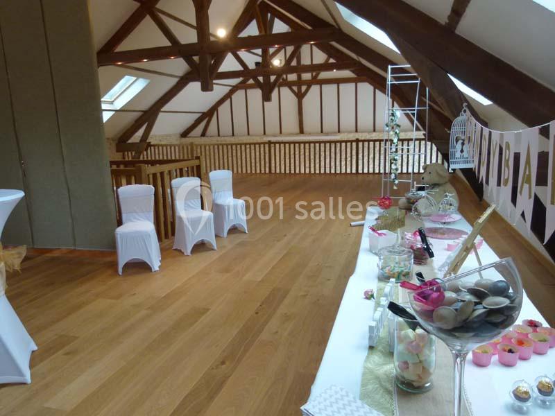 Salle avec poutres apparentes, parquet en bois, chaises blanches et table décorée pour un événement festif.