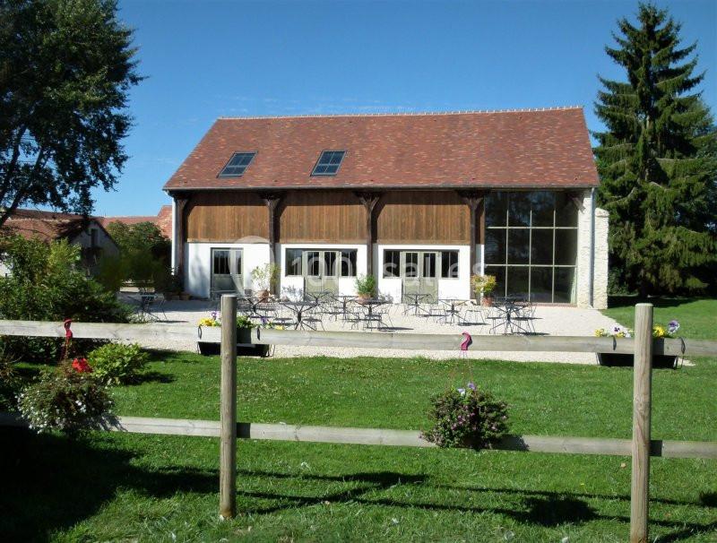 Bâtiment rénové avec façade en bois et grandes baies vitrées, entouré d'une terrasse aménagée et d'un jardin verdoyant.