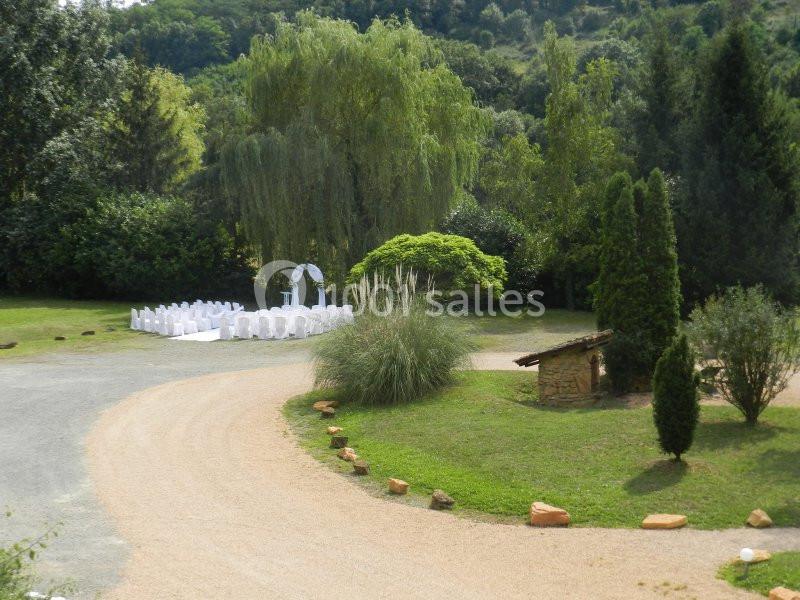 Cérémonie en plein air avec des chaises blanches disposées en cercle devant une arche, entourée de verdure.