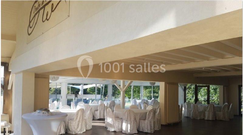 Salle de réception lumineuse avec tables rondes dressées de nappes blanches et vue sur un espace extérieur verdoyant.