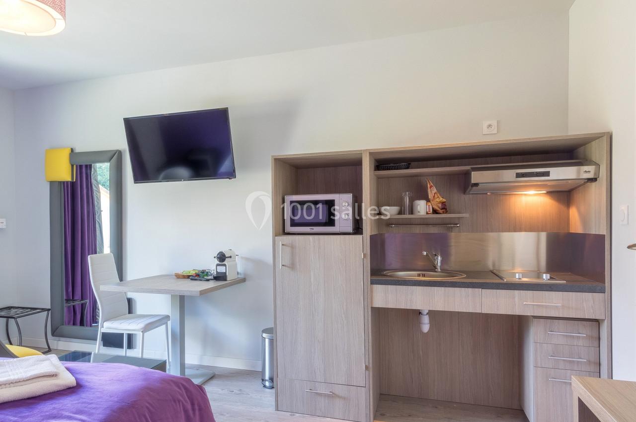 Coin kitchenette dans une chambre avec micro-ondes, évier, rangements, table, chaise et télévision murale.