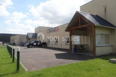 Bâtiment beige à un étage avec des fenêtres blanches, entouré d'une pelouse et d'arbustes, sous un ciel partiellement…