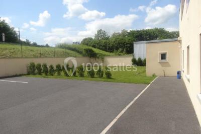 Bâtiment beige à un étage avec des fenêtres blanches, entouré d'une pelouse et d'arbustes, sous un ciel partiellement…