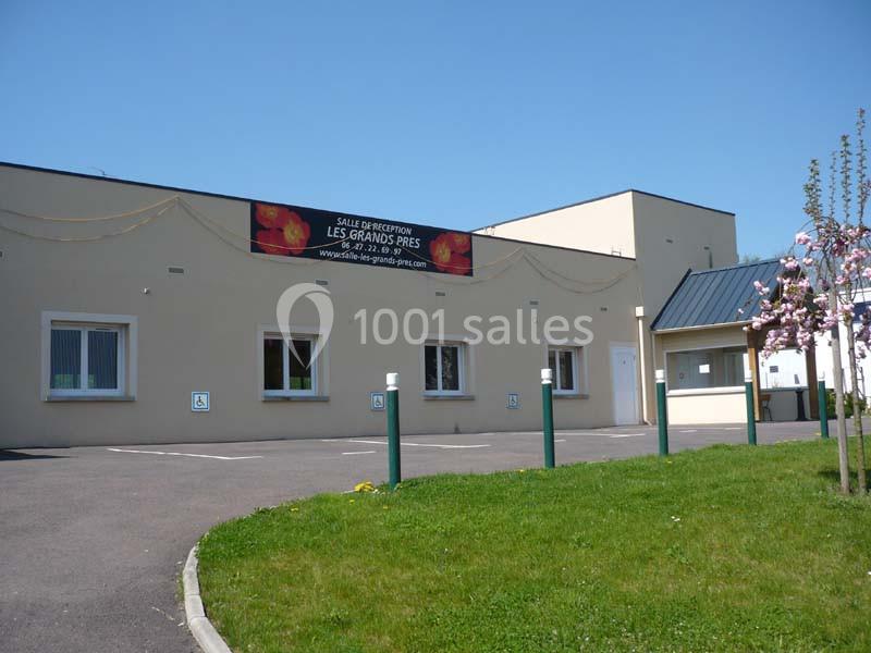 Façade d'une salle de réception beige avec parking et pelouse au premier plan.