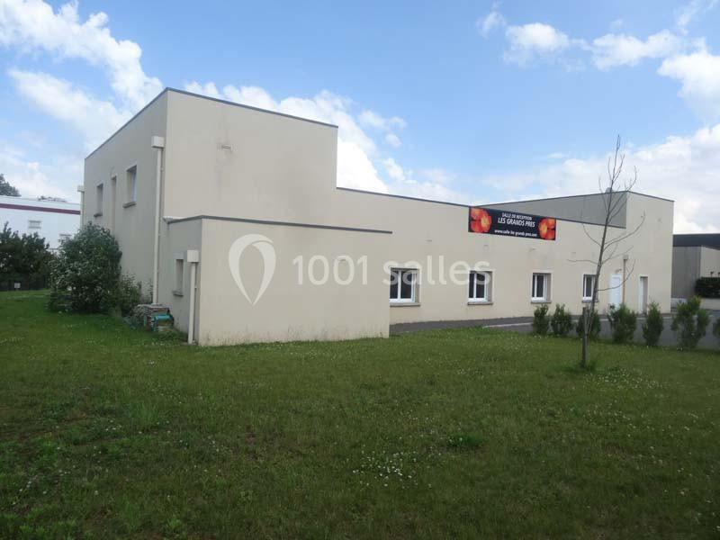 Bâtiment beige à un étage avec des fenêtres blanches, entouré d'une pelouse et d'arbustes, sous un ciel partiellement…