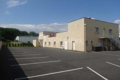 Bâtiment beige à un étage avec des fenêtres blanches, entouré d'une pelouse et d'arbustes, sous un ciel partiellement…