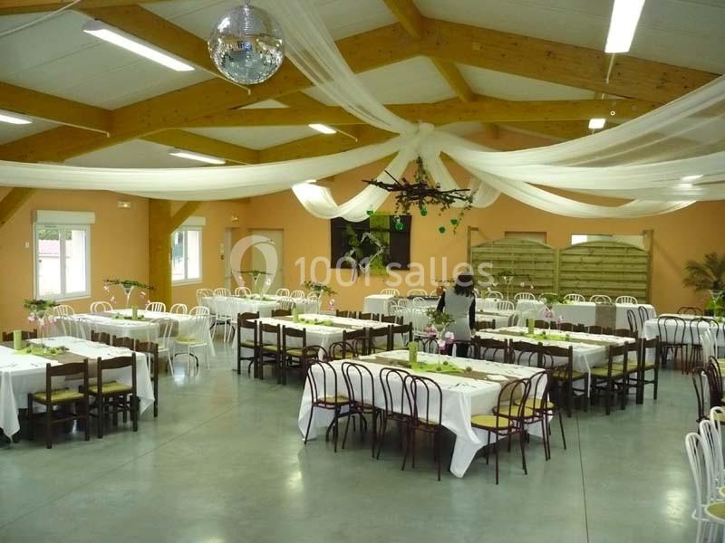 Salle de réception décorée avec des tables dressées, des chaises blanches et en bois, et un plafond orné de voilages blancs.
