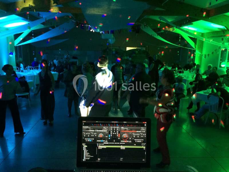 Des personnes dansent dans une salle éclairée par des lumières colorées, vue depuis une table de mixage.