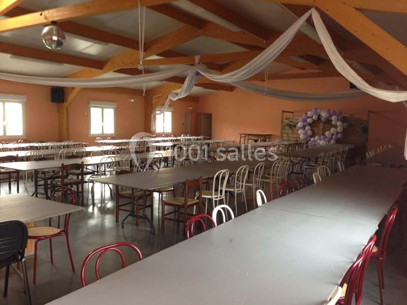 Salle de réception avec de longues tables alignées, des chaises variées et une décoration en voilages et ballons.