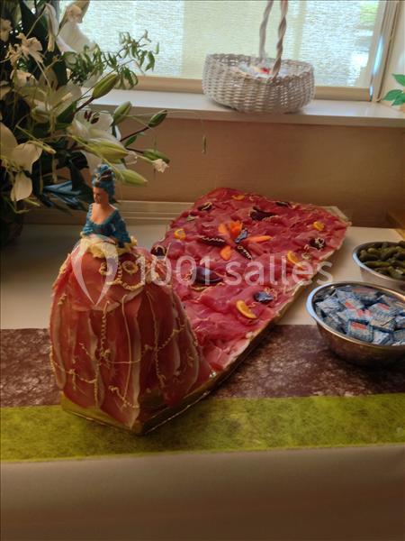 Présentoir de charcuterie en forme de robe avec une figurine, accompagné de condiments et décorations florales.