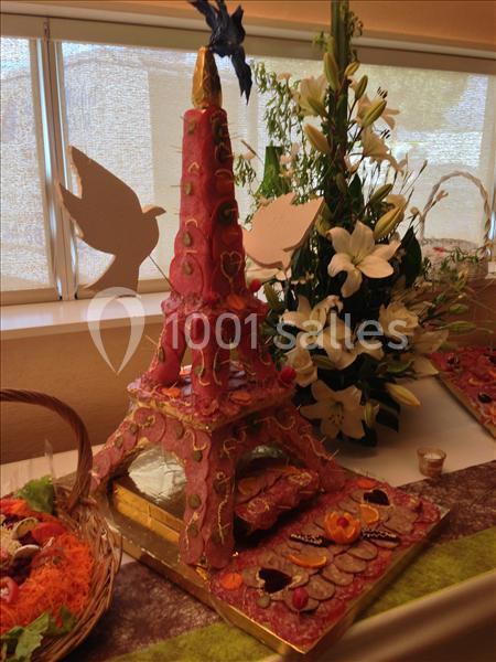 Tour Eiffel en pièce montée rose décorée de motifs dorés, entourée de fleurs blanches et d'éléments de décoration.