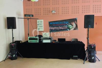 Bâtiment beige à un étage avec des fenêtres blanches, entouré d'une pelouse et d'arbustes, sous un ciel partiellement…