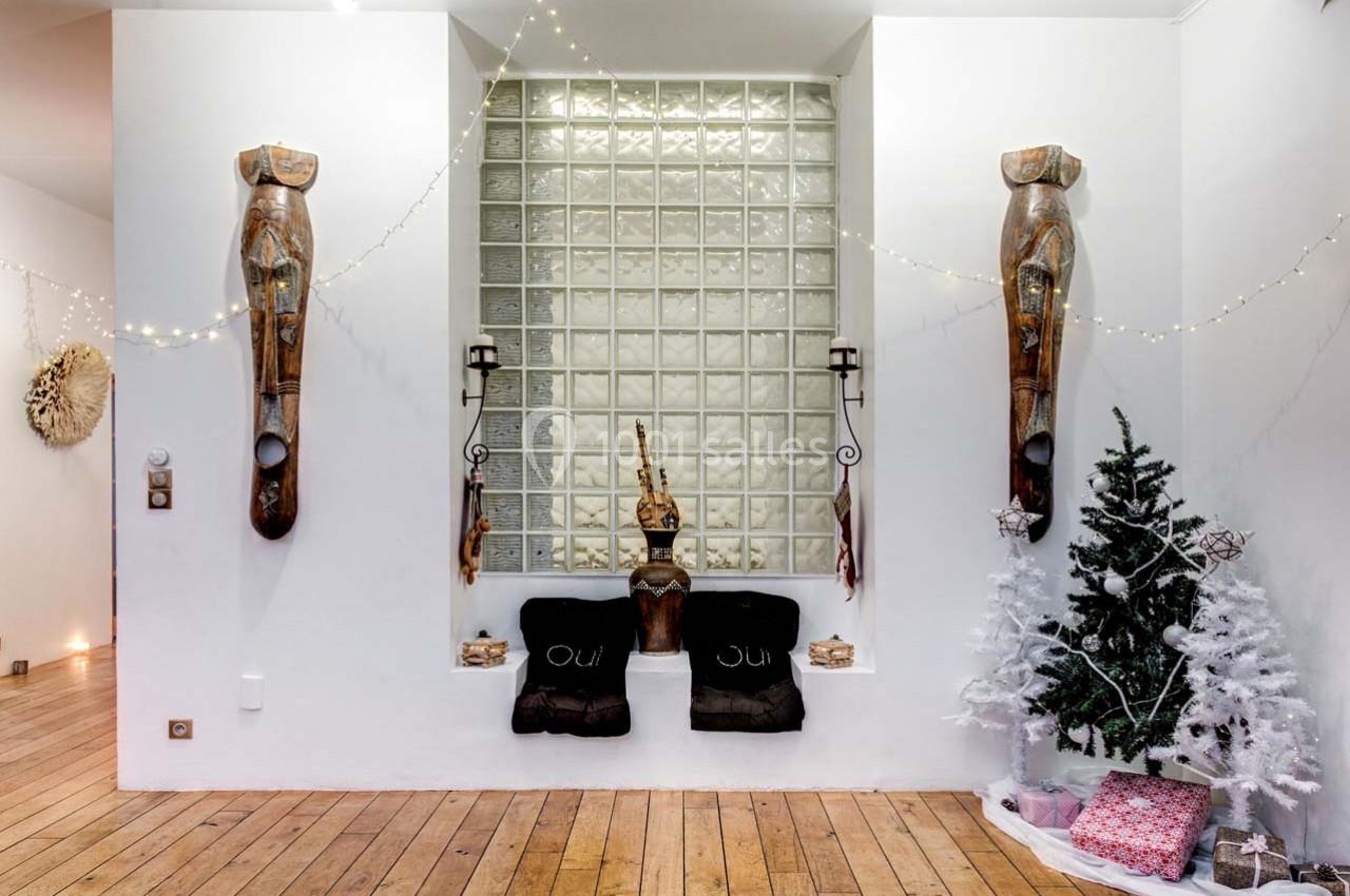 Niche murale décorée avec sculptures en bois, coussins noirs, sapin blanc et guirlandes lumineuses.