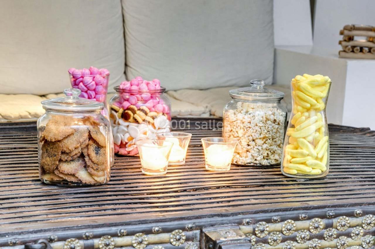 Bocaux remplis de biscuits, bonbons, pop-corn et snacks salés disposés sur une table avec des bougies allumées.