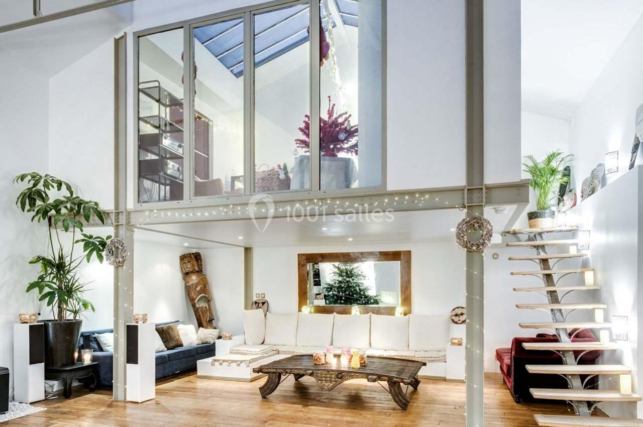 Salon lumineux avec mezzanine, mobilier en bois, canapé blanc, plantes et décoration moderne dans un espace ouvert.