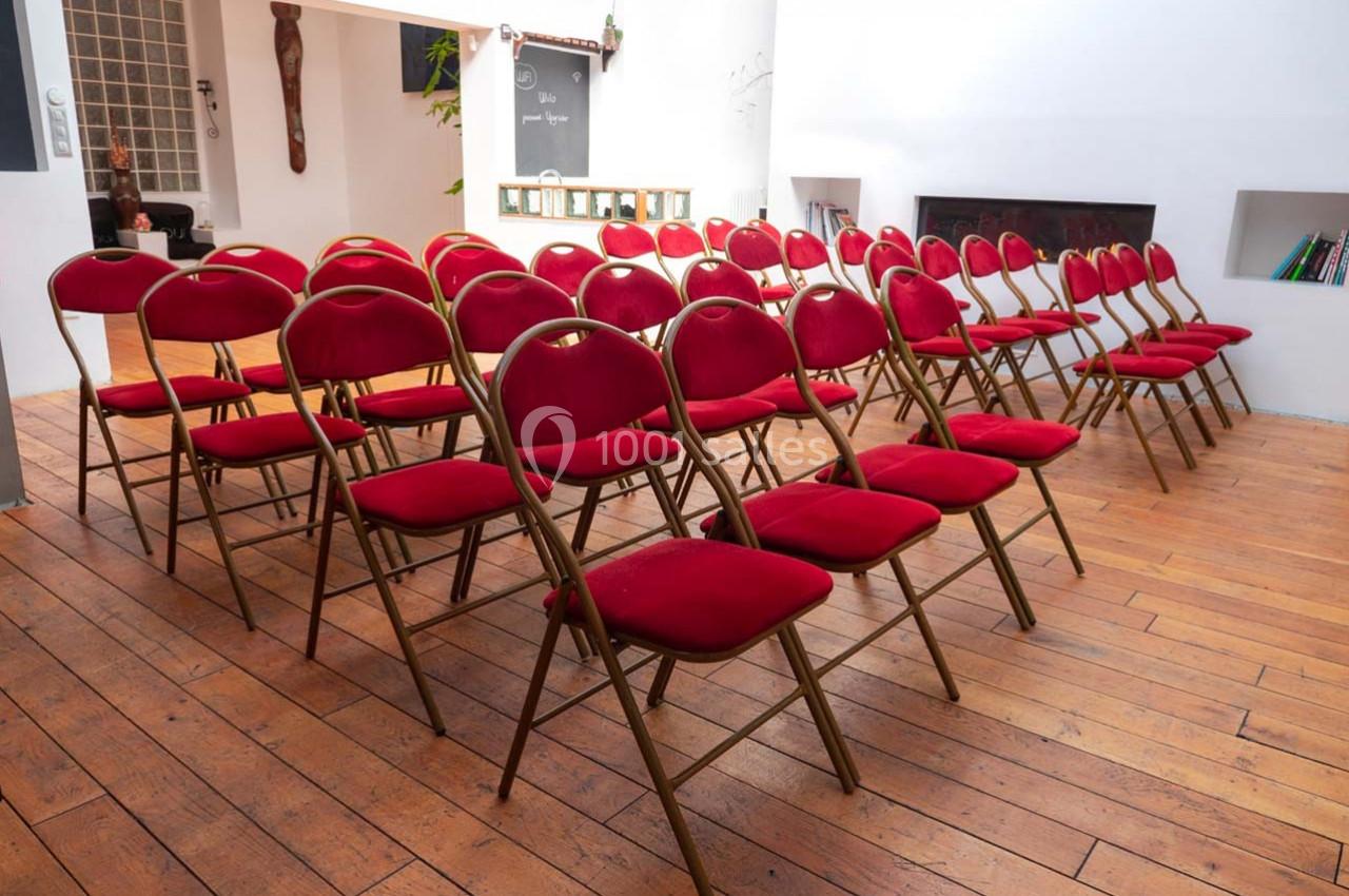 Rangées de chaises pliantes rouges alignées dans une salle lumineuse au sol en bois.