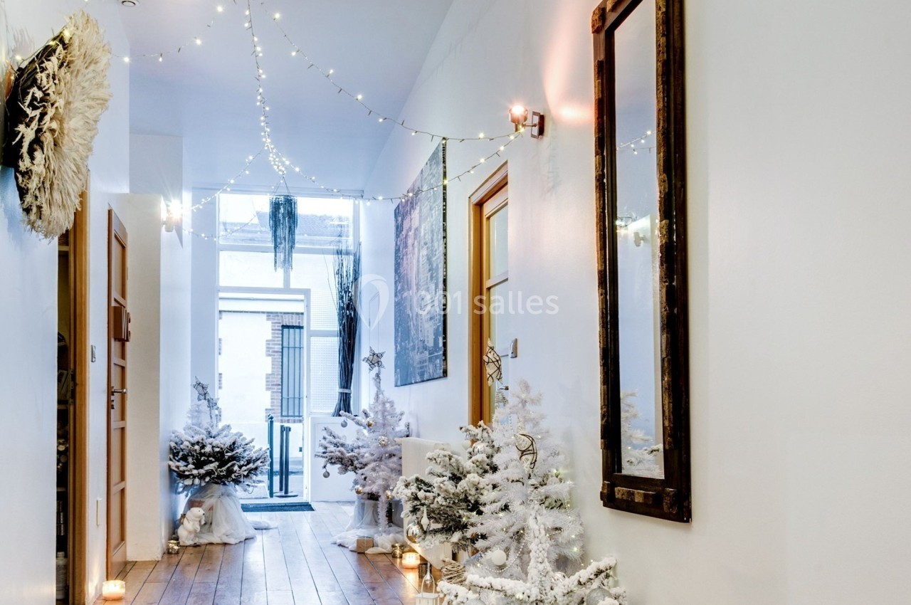 Couloir décoré pour Noël avec guirlandes lumineuses, sapins enneigés, lanternes blanches et sol en bois clair.