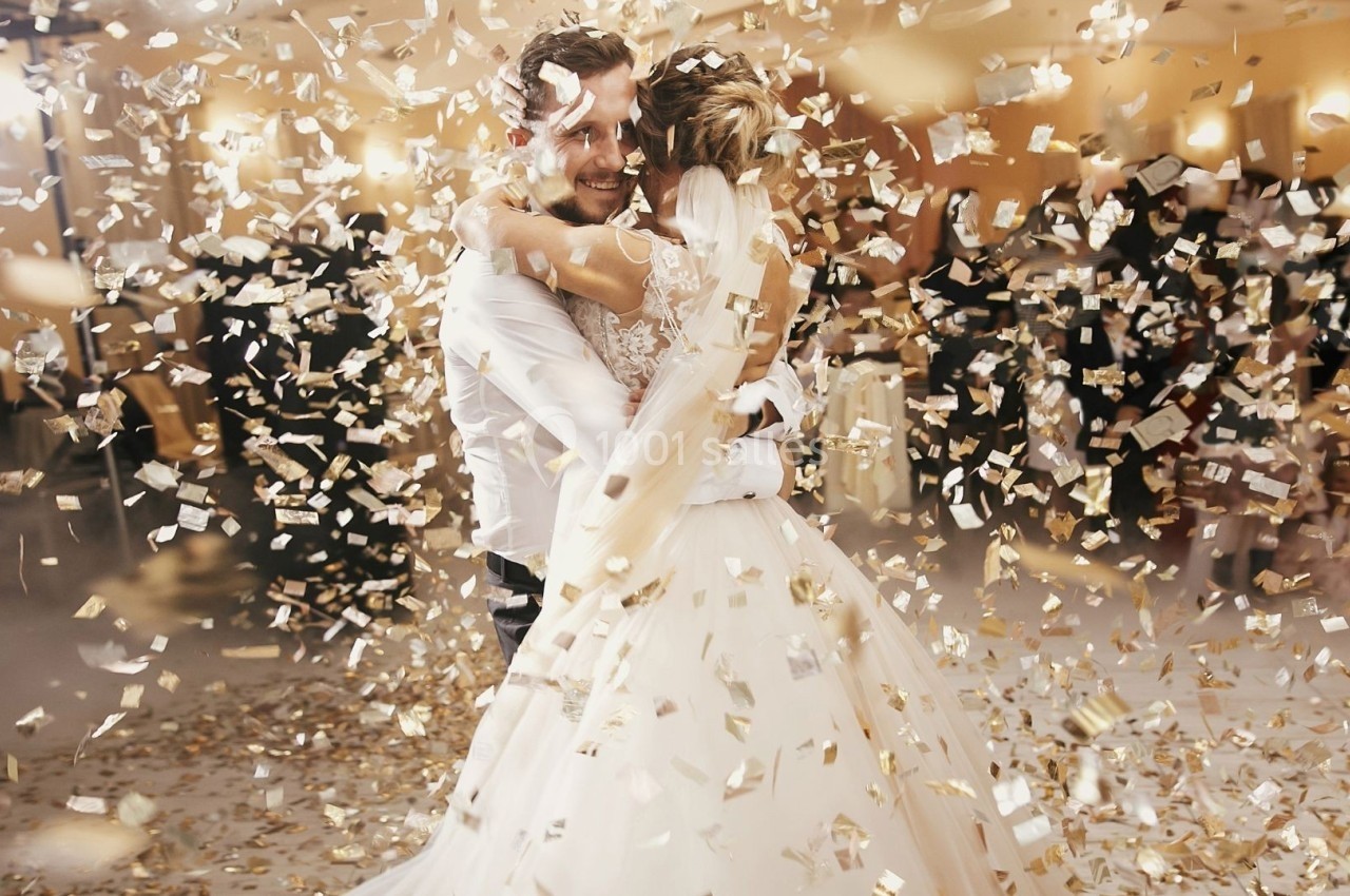 Un couple danse au milieu de confettis dorés lors d'une fête dans une salle éclairée.