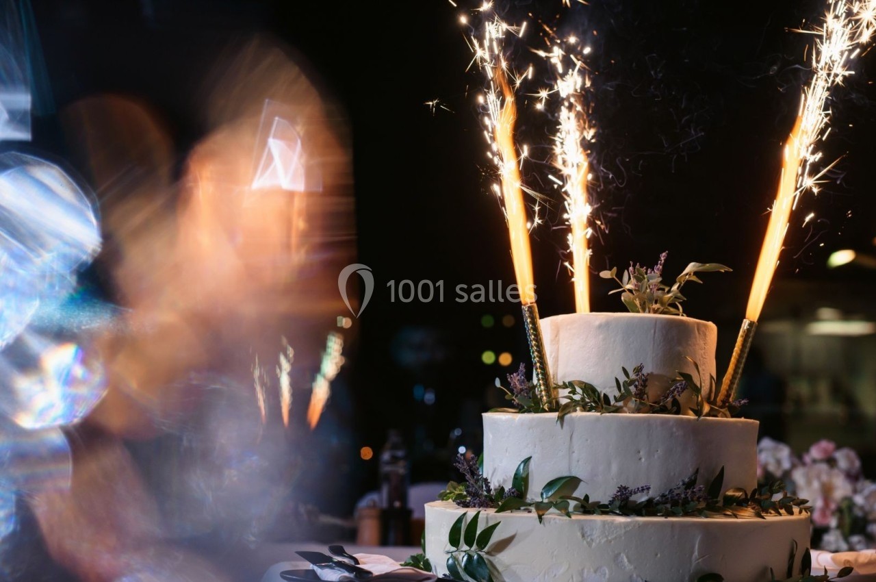 Gâteau de mariage à trois étages décoré de feuillages et de fleurs, avec des cierges magiques allumés au sommet.