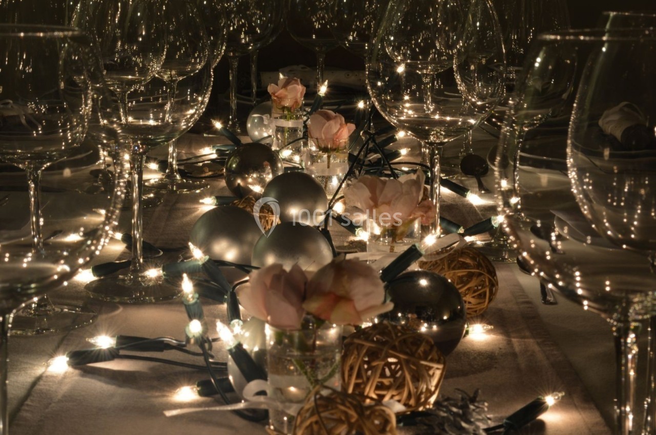 Table décorée avec des guirlandes lumineuses, des fleurs roses, des boules argentées et des verres à pied.