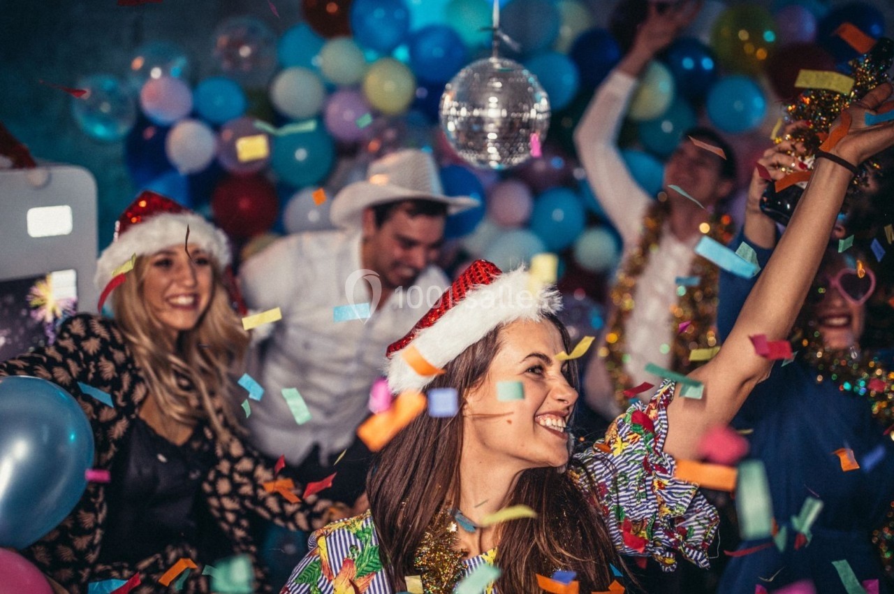 Personnes portant des chapeaux de Noël dansant et célébrant entourées de confettis, ballons et une boule disco.