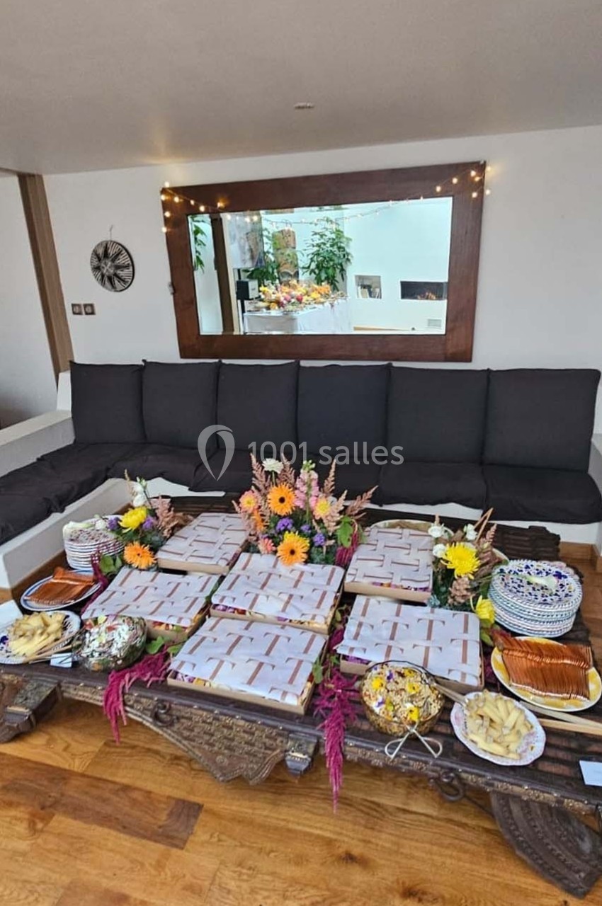Plateau en bois avec des boîtes alignées, entouré de fleurs et de plats variés, dans un salon lumineux.