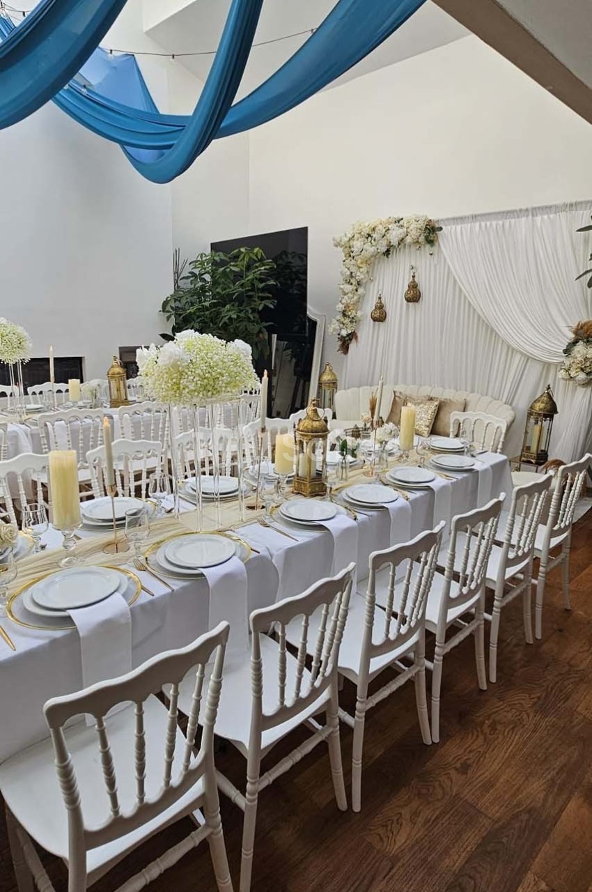 Salle décorée pour un événement avec tables alignées, nappes blanches, bougies, fleurs et drapés bleus suspendus.